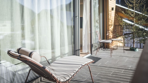 Un área de estar exterior moderna con una silla lounge y una mesita, con vistas a una terraza con barandilla y al paisaje circundante.