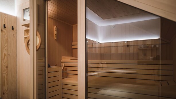 Un espai de sauna amb seients de fusta, una porta de vidre i una làmpada al sostre.