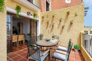 Une terrasse avec une table ronde et des chaises, des plantes en pot accrochées au mur et une vue sur la rue.