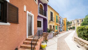 Une rangée de bâtiments aux couleurs vives, avec un trottoir pavé et des marches menant à l’entrée.