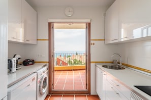 Una cuina compacta amb rentadora, un rentaplat i vista al mar.