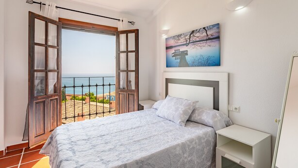 Une chambre à coucher avec un lit, une table de chevet, un tableau et une vue sur la mer par une porte ouverte.