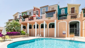 Une piscine avec des chaises longues, un palmier et des bâtiments aux couleurs vives en arrière-plan.
