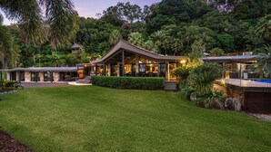 Une maison moderne dotée d’un grand patio, entourée d’une végétation luxuriante et agrémentée d’une piscine.