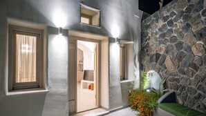 Fachada moderna con pared de piedra, un banco verde y una puerta de entrada a un espacio interior.