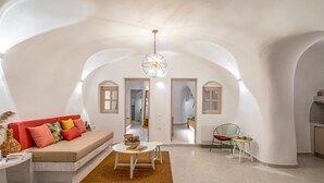 Un salón amplio con un sofá, una mesa redonda y una silla. Hay puertas arqueadas que dan a otras habitaciones.