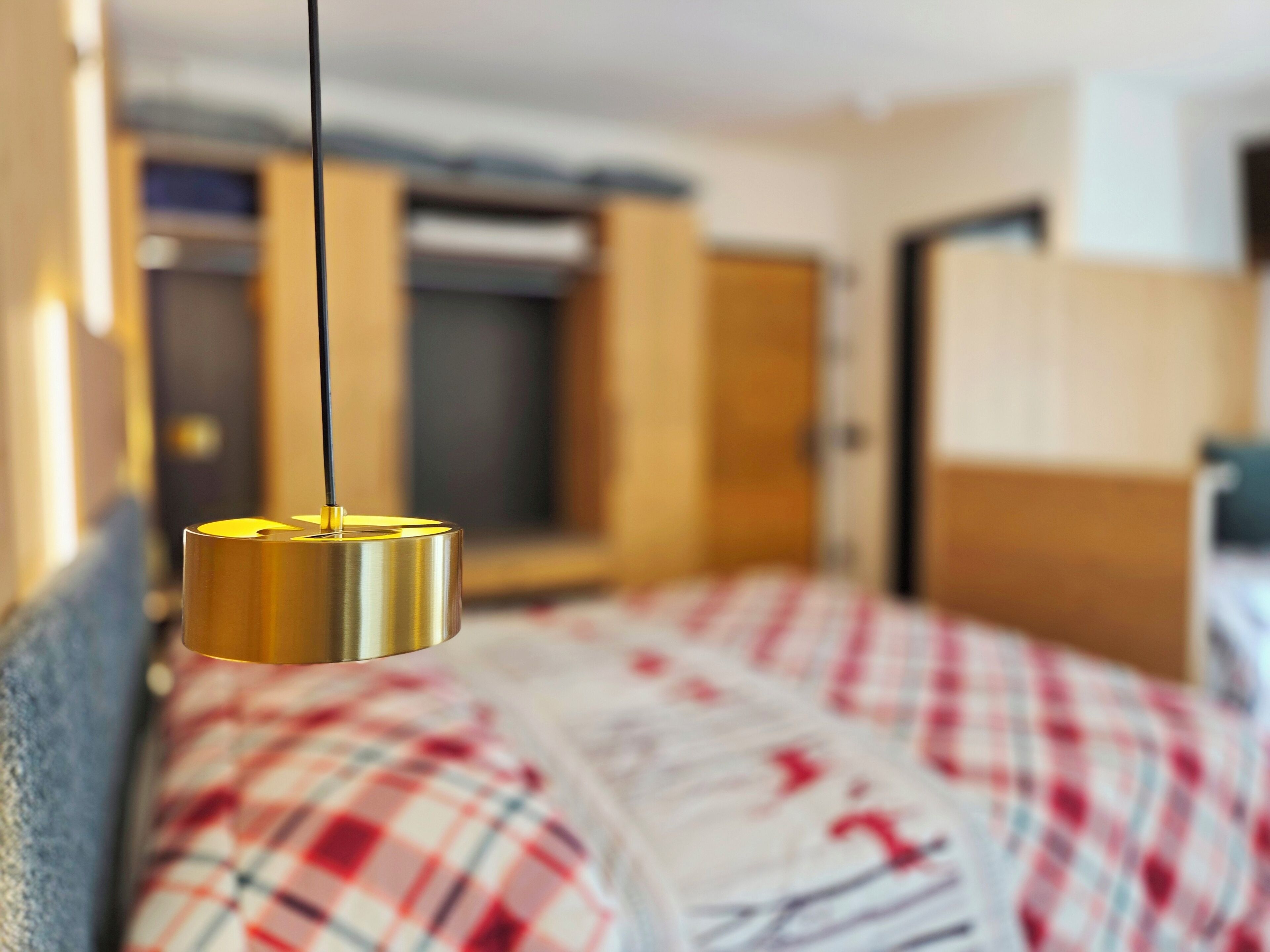 Un lit recouvert d’une couverture à carreaux, une lampe suspendue et une armoire en arrière-plan.