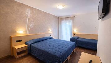Habitación de hotel con dos camas, una mesita de noche de madera, una pequeña mesa y un televisor montado en la pared.