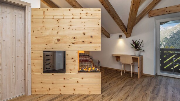 A modern interior with exposed wooden beams, a fireplace, a desk, and a view of mountains. - Pier Hotel (Andalo)