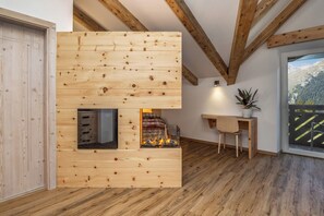 A modern interior with exposed wooden beams, a fireplace, a desk, and a view of mountains. - Pier Hotel (Andalo)