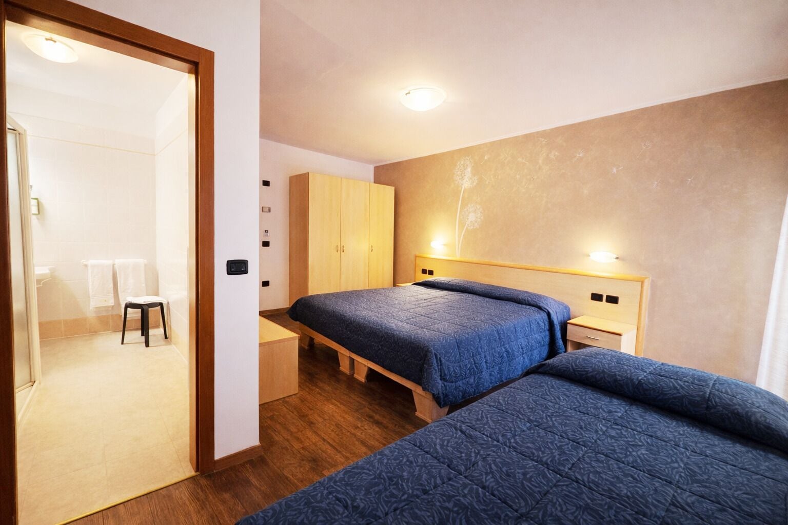 Un dormitorio con dos camas, un armario de madera y un taburete pequeño.