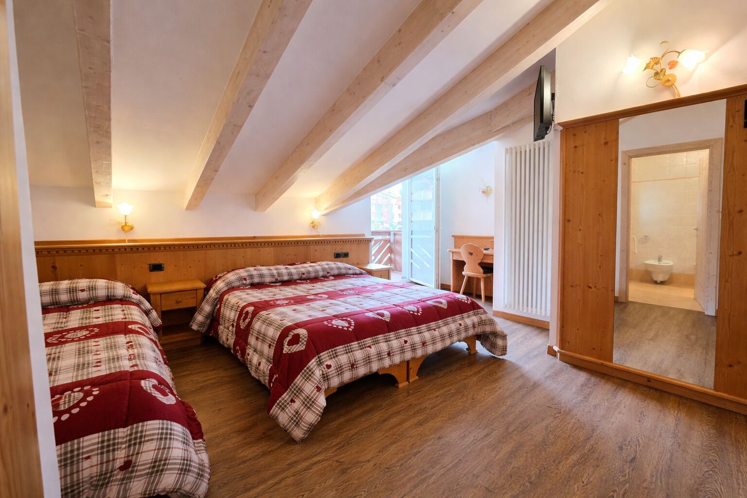 A room with two beds, a wooden ceiling, a desk, and a bathroom.