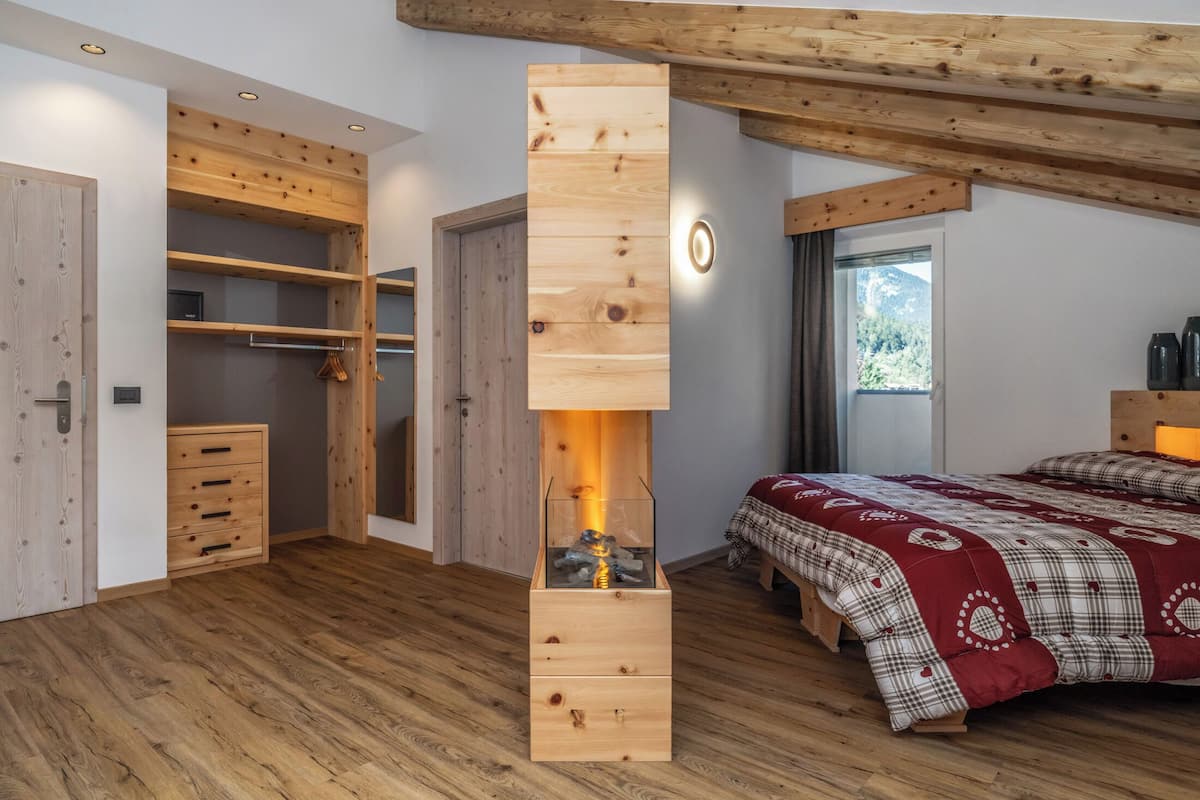 Une chambre avec une armoire en bois, un lit recouvert d’une couverture à carreaux et une cheminée.