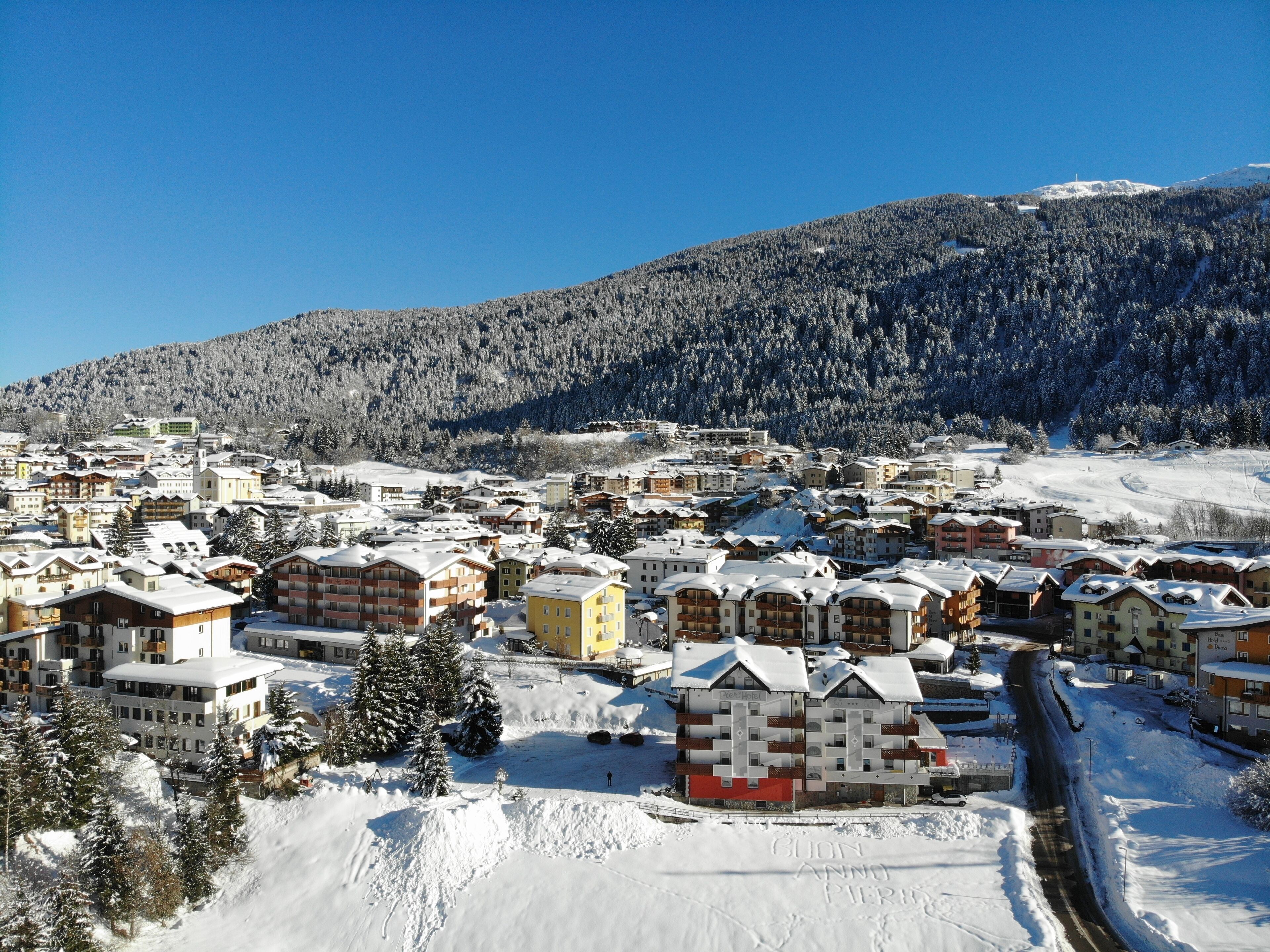 Une ville enneigée, avec des immeubles à plusieurs étages, une piste de ski en arrière-plan et un ciel bleu dégagé.