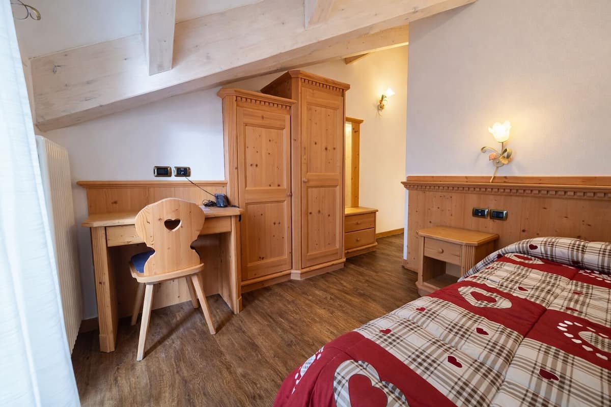 Une chambre à coucher comprenant un bureau en bois, une chaise, une armoire, une table de chevet et un lit recouvert d’une couverture à carreaux.