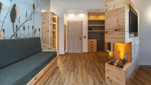 A room with a wooden floor, a sofa, a TV mounted on a wooden wall, and a fireplace. - Pier Hotel (Andalo)