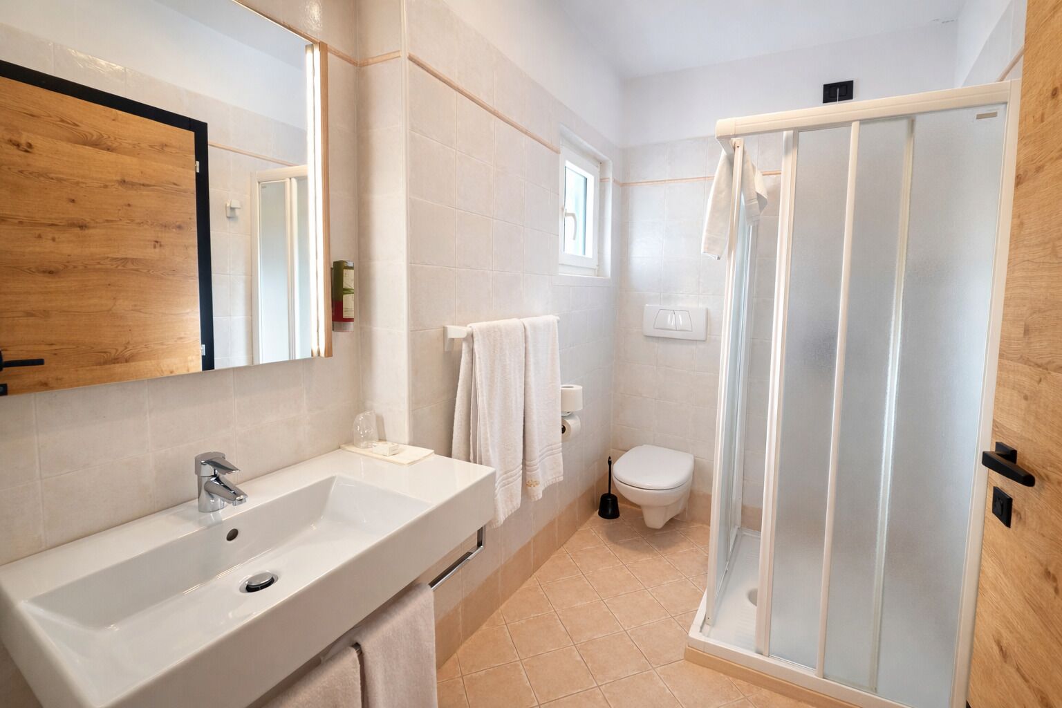 A bathroom with a white sink, mirror, toilet, and shower enclosure.