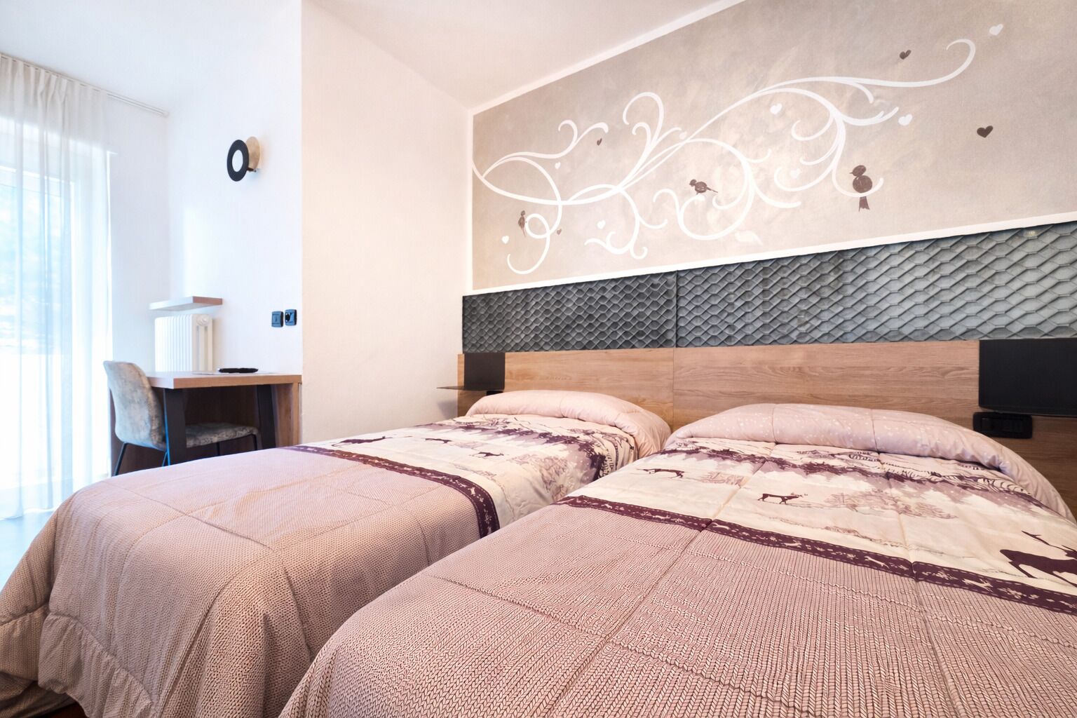 A hotel room with two beds, a desk, and a decorative wall.