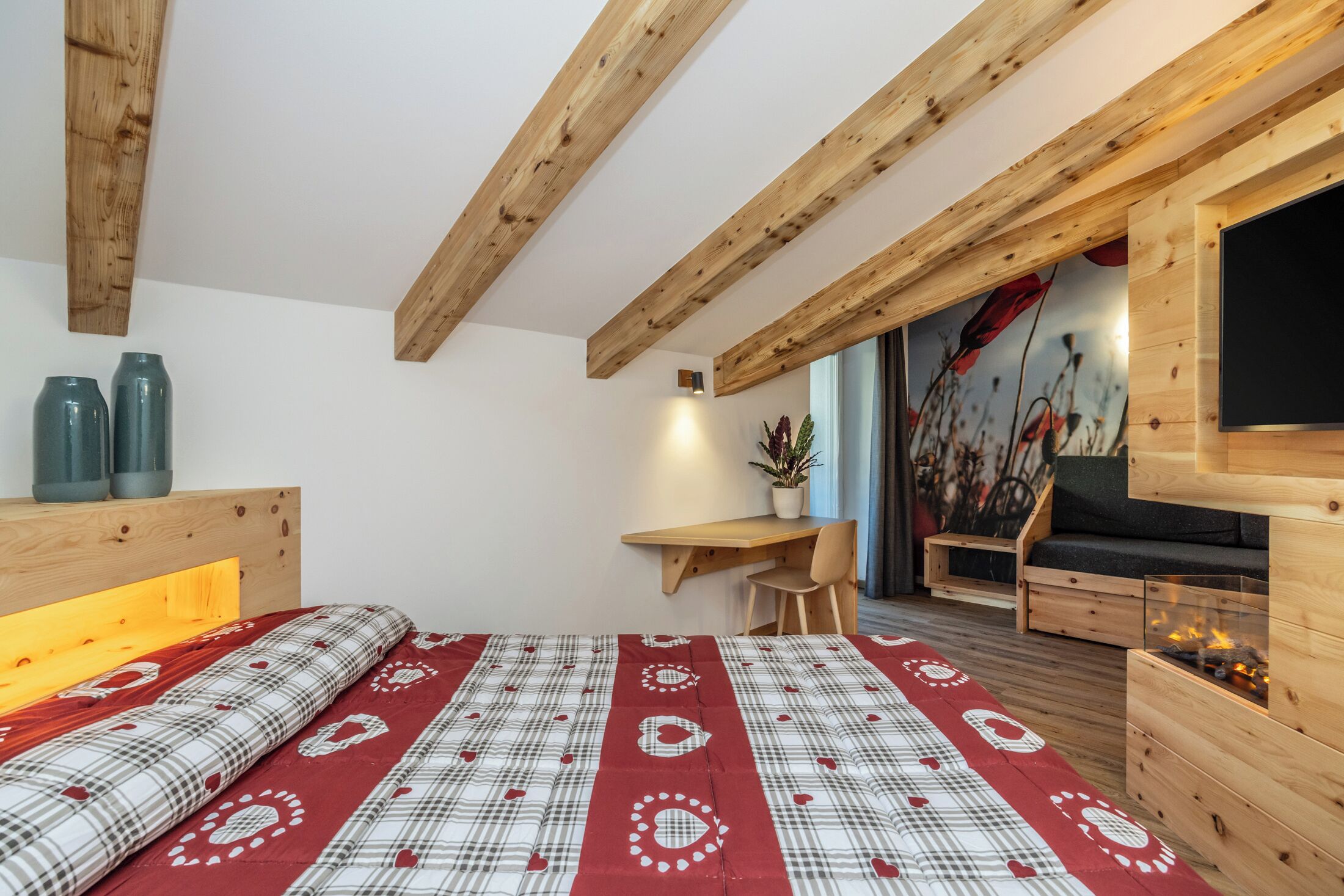 Un dormitorio con cama, vigas de madera, un escritorio, un sofá y una chimenea.