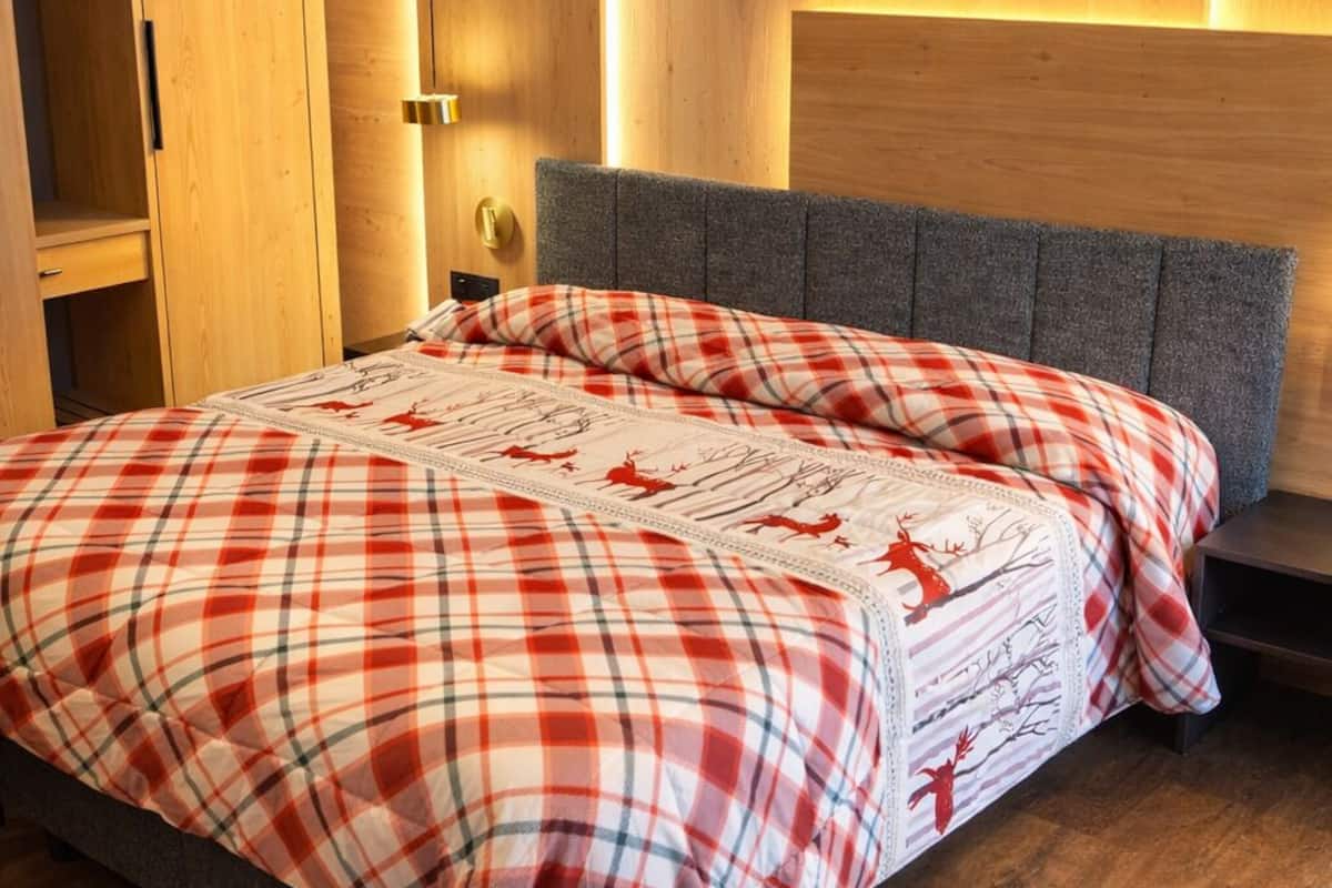 Un lit avec une couvre-lit à carreaux, une armoire en bois et une tête de lit dotée d’un éclairage intégré.