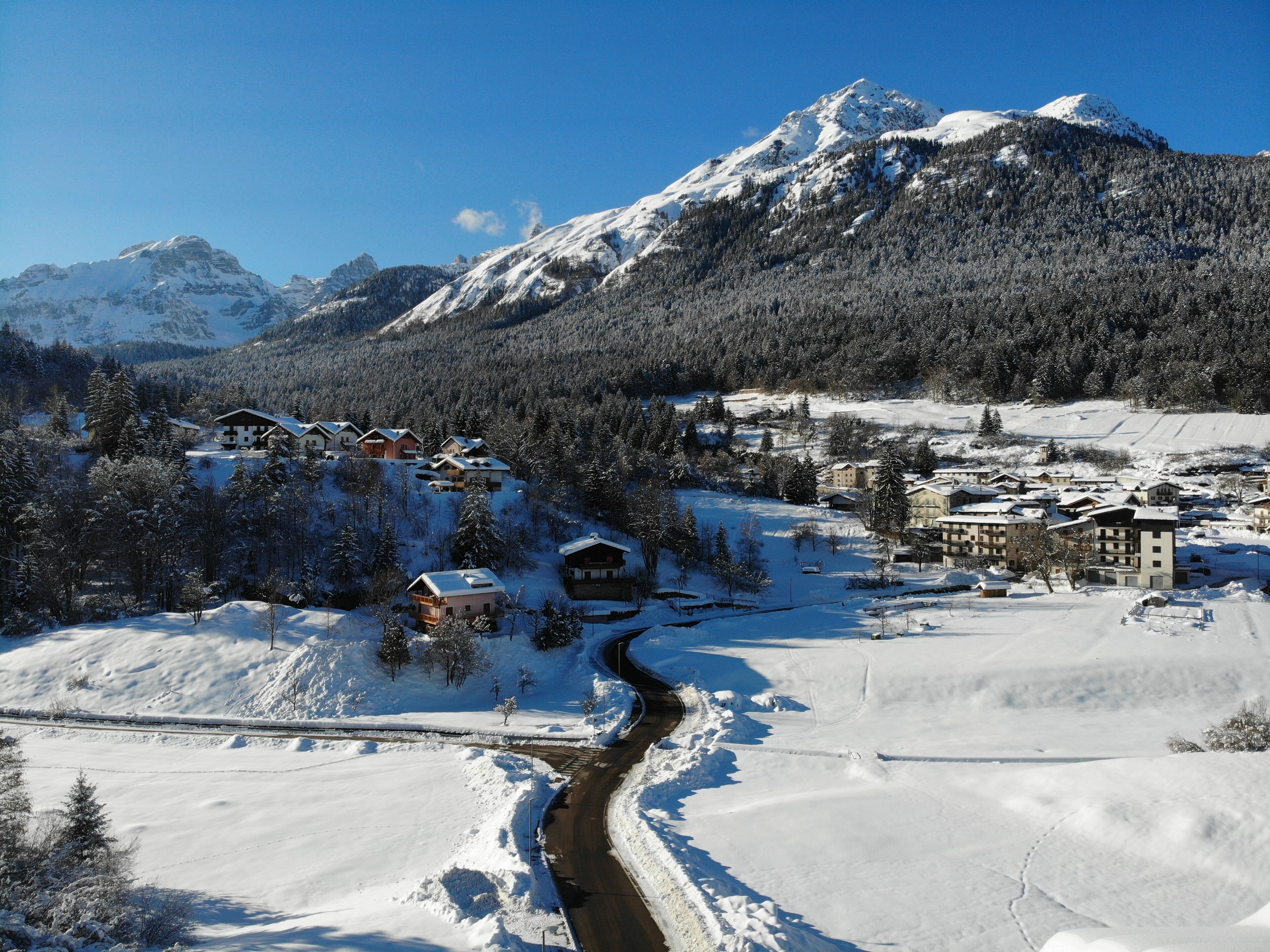 Un pueblo de montaña cubierto de nieve con edificios de estilo chalete, un camino serpenteante y un río.