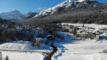 Un pueblo de montaña cubierto de nieve con edificios de estilo chalete, un camino serpenteante y un río.