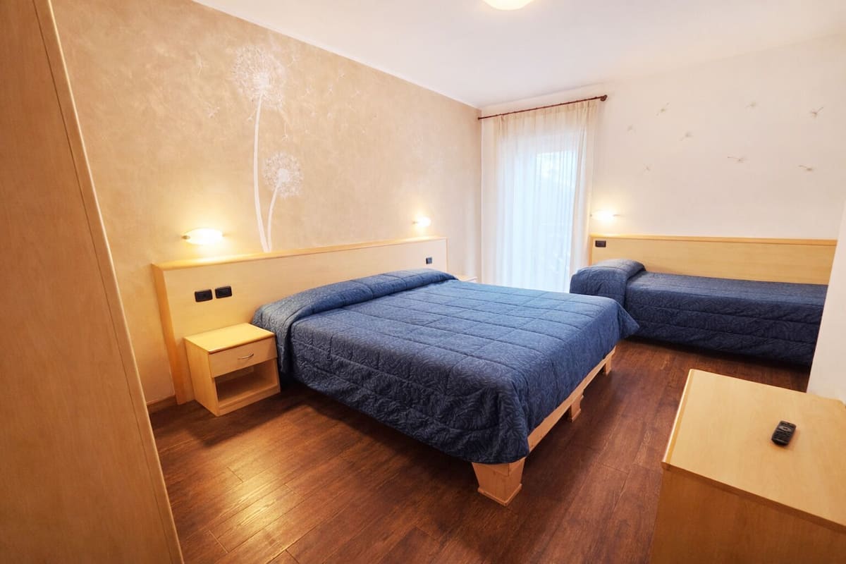 Une chambre d’hôtel avec un grand lit, deux tables de chevet, un petit bureau et une fenêtre avec des rideaux.