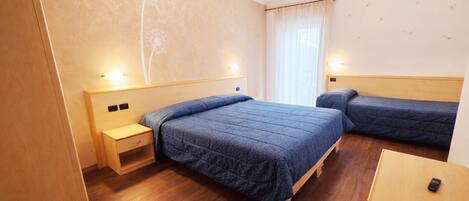 A hotel room with a large bed, two bedside tables, a small desk, and a window with curtains.