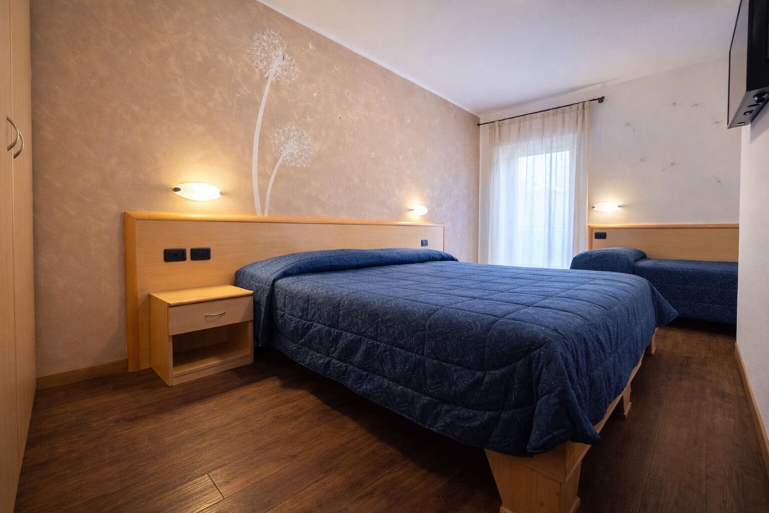 Une chambre d’hôtel avec deux lits, des têtes de lit en bois, des tables de chevet et un mur décoré d’un motif de pissenlit.