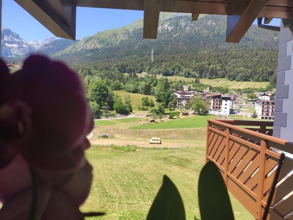 Un balcon offrant une vue sur un paysage montagneux, un champ verdoyant et plusieurs bâtiments situés au loin.