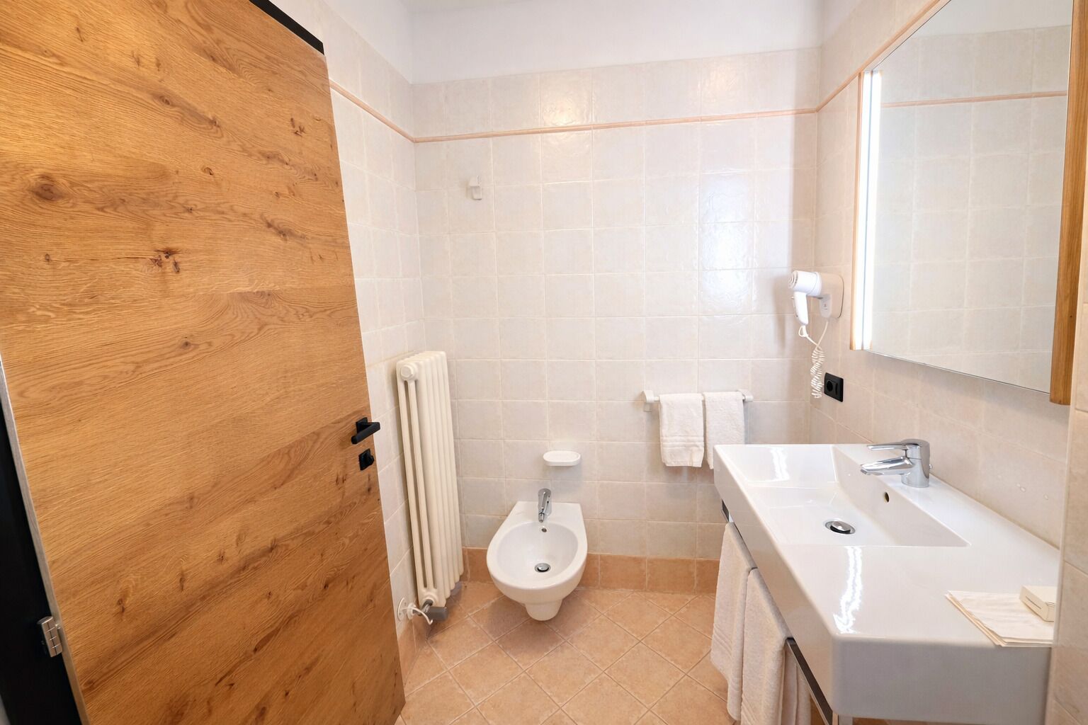 A bathroom with a wooden door, a toilet, a sink, a mirror, and a towel rack.