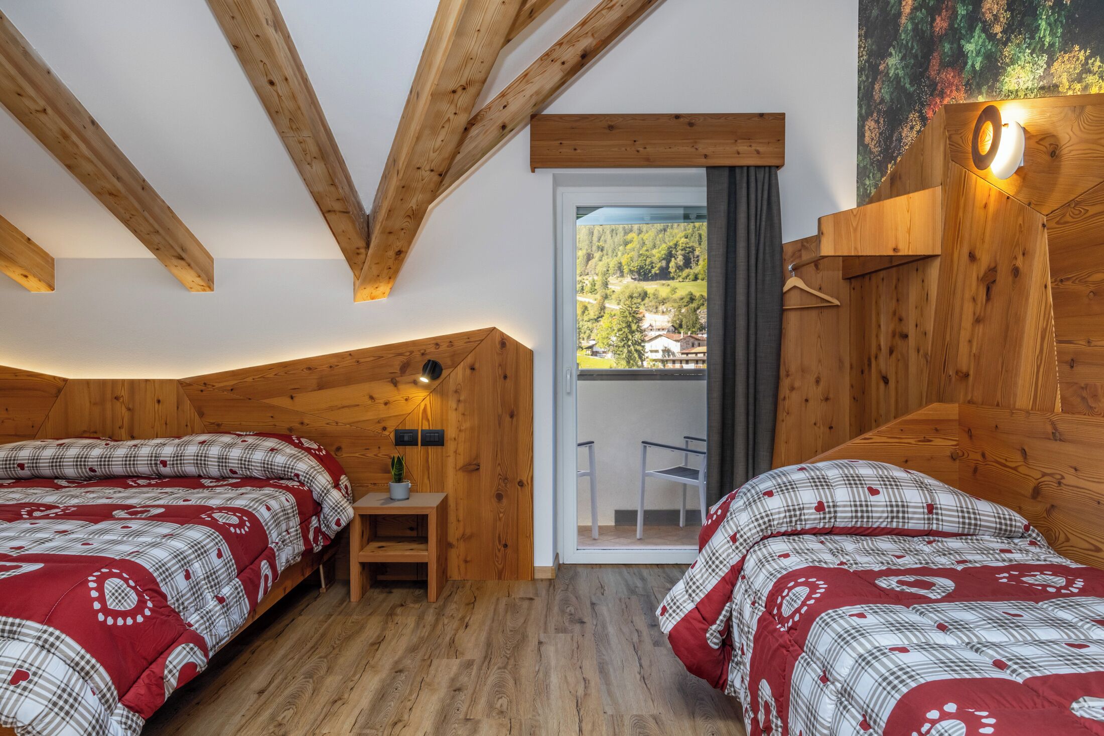 Una habitación con vigas de madera, una cama con colcha a cuadros, una pequeña mesa con una planta y vistas a través de un ventanal.