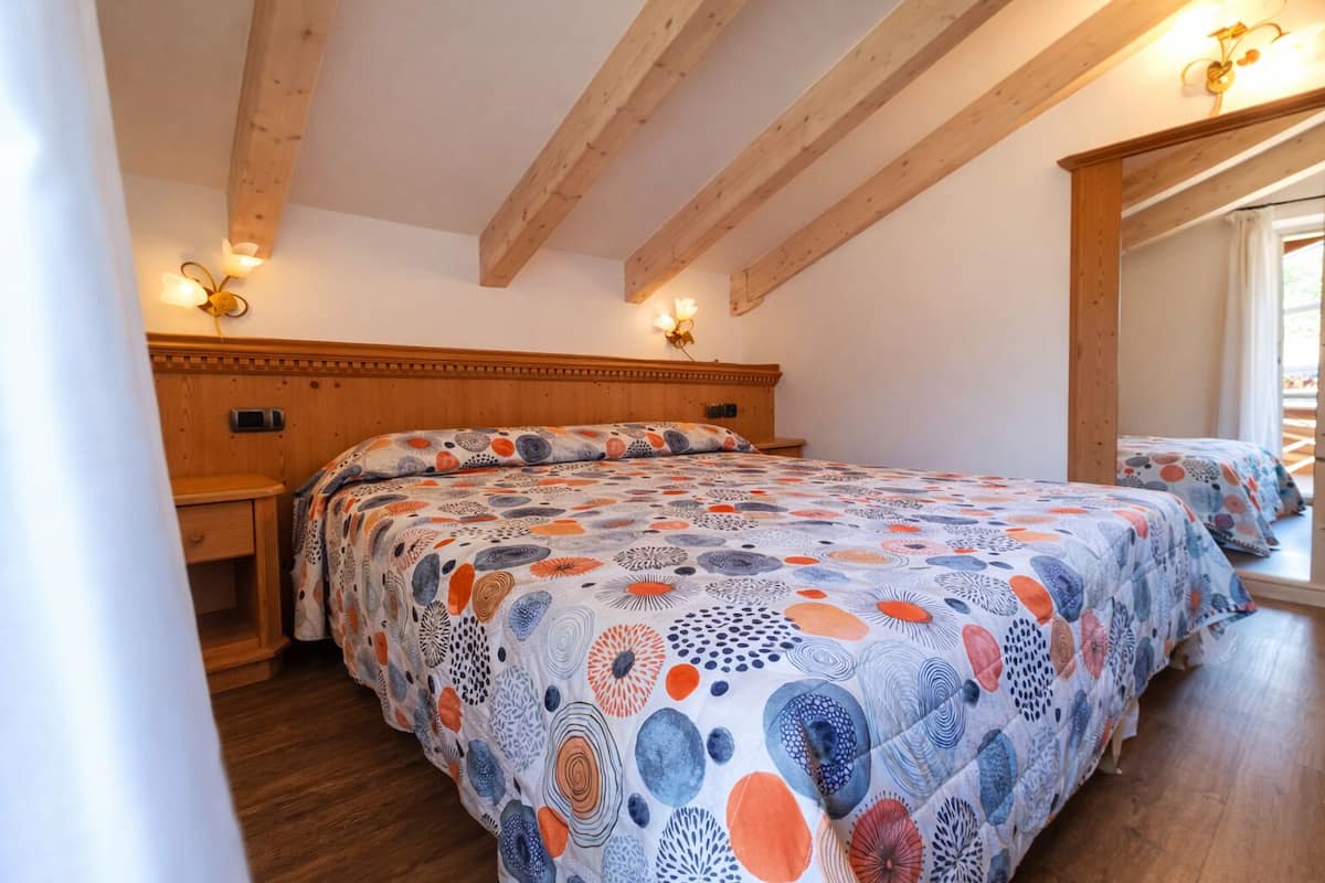 Une chambre avec un plafond en bois, un grand lit recouvert d’une couvre-lit à motifs, des lampes de chevet et une table de chevet.