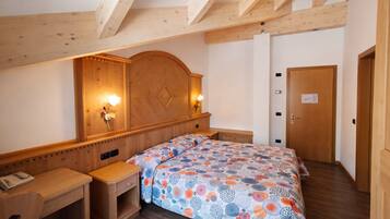 Ein Hotelzimmer mit einem hölzernen Kopfende, einem Bett mit einem gemusterten Bettbezug, einem Nachttisch mit Telefon und einer Holztür.