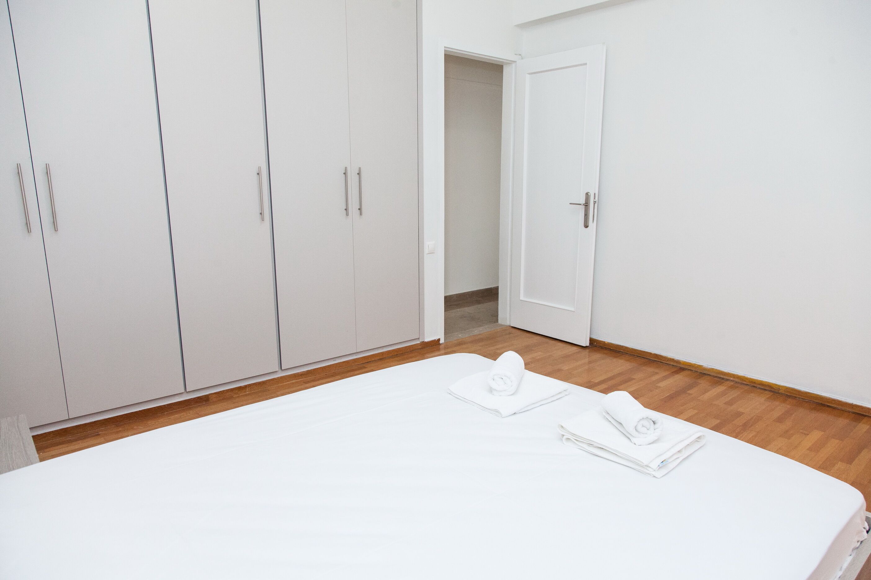 A bedroom with a large bed, white wardrobe, and a door leading to another room.