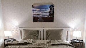 A bedroom with a large bed, two bedside tables, a wall-mounted picture, and wooden flooring.