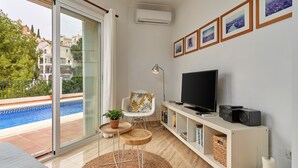 A modern living room with a TV, bookshelf, and a view of a swimming pool. - Holiday Apartment with Private Pool near the Beach with 2 Terraces and Wi-Fi (Nerja)