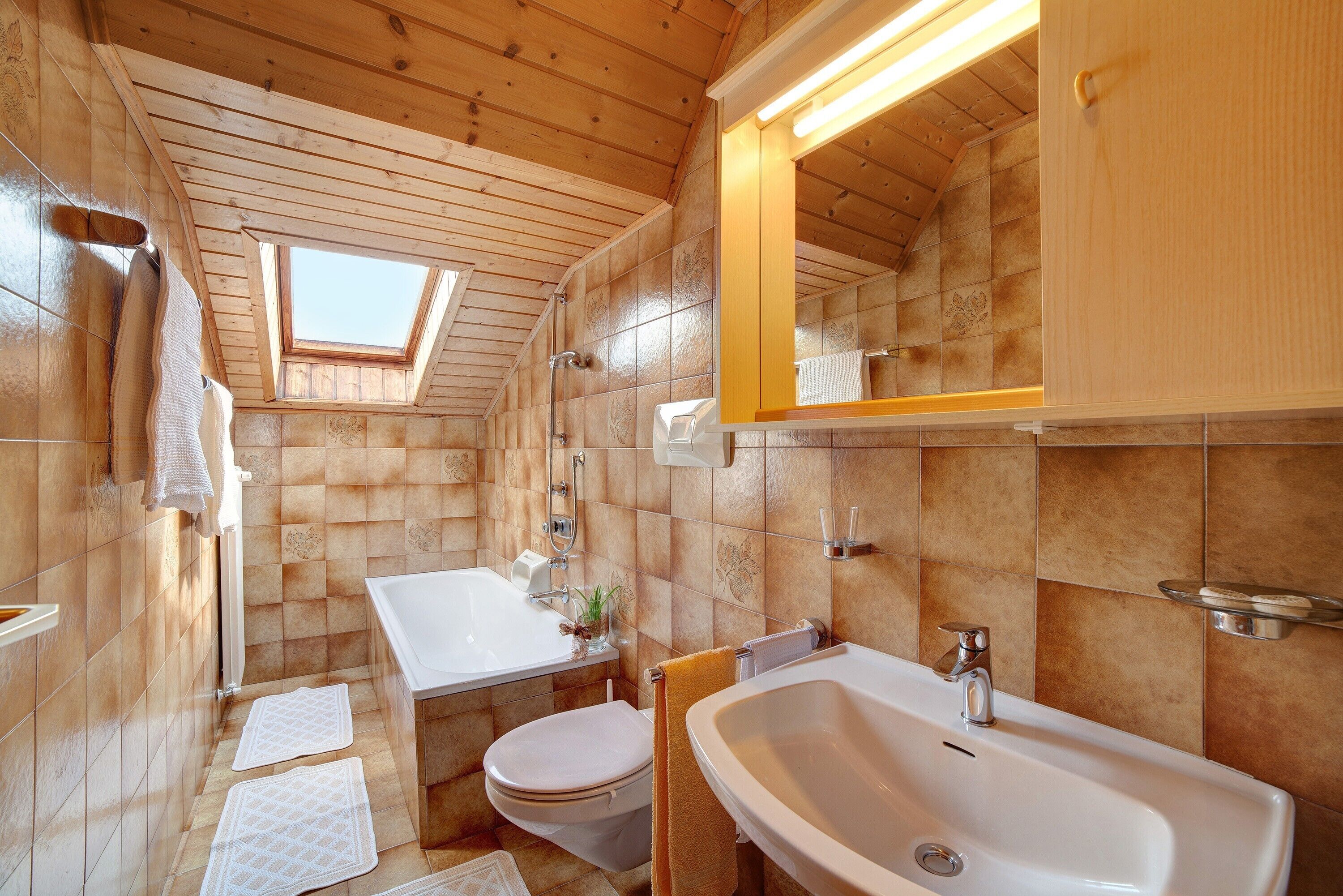 A wooden interior with a skylight, a white bathtub, a toilet, and a sink.