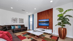 Una sala de estar con un sofá de cuero marrón, una mesa de centro blanca y un televisor de pantalla plana grande montado en una pared de madera.