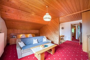 Ein gemütliches Zimmer mit Holzbalkendecke, einer Couch, einem Tisch und einem roten Teppich.