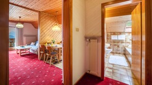 A room with a wooden ceiling, a dining area with a table and chairs, a sofa, and a red carpet. - Holiday Apartment 'Sankt Corbinian 4' with Mountain View, Balcony, Shared Garden & Wi-Fi (Kuens)