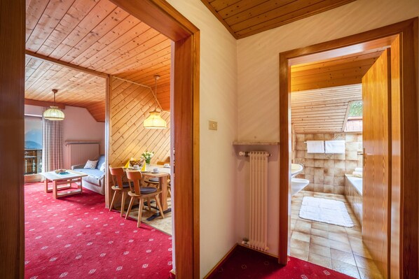 Ein Zimmer mit Holzboden, einem Essbereich mit Tisch und Stühlen, einer Couch und einem roten Teppich.