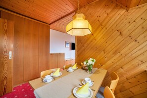 A dining area with a wooden table set for four, a hanging light fixture, and a view of a wooden ceiling.