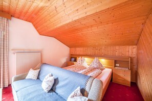 Une pièce chaleureuse avec un plafond en bois, un lit recouvert d’une literie à motifs floraux, une table de chevet et un radiateur.