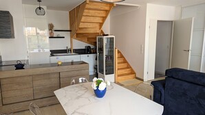 A modern kitchen with a wooden staircase, a dining area with a marble table, and a dark blue sofa. - Central Arcachon - Bright 3* Duplex T3 with Balcony, Parking, and Modern Amenities (Arcachon)