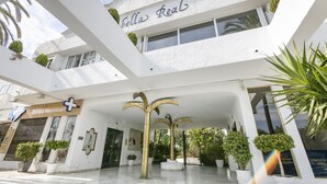 A white building with the sign "Bella Real" and a veterinary center sign. There are potted plants and a palm tree in the entrance area.