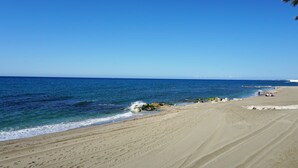A beach with clear blue water, sandy shore, and some rocks.