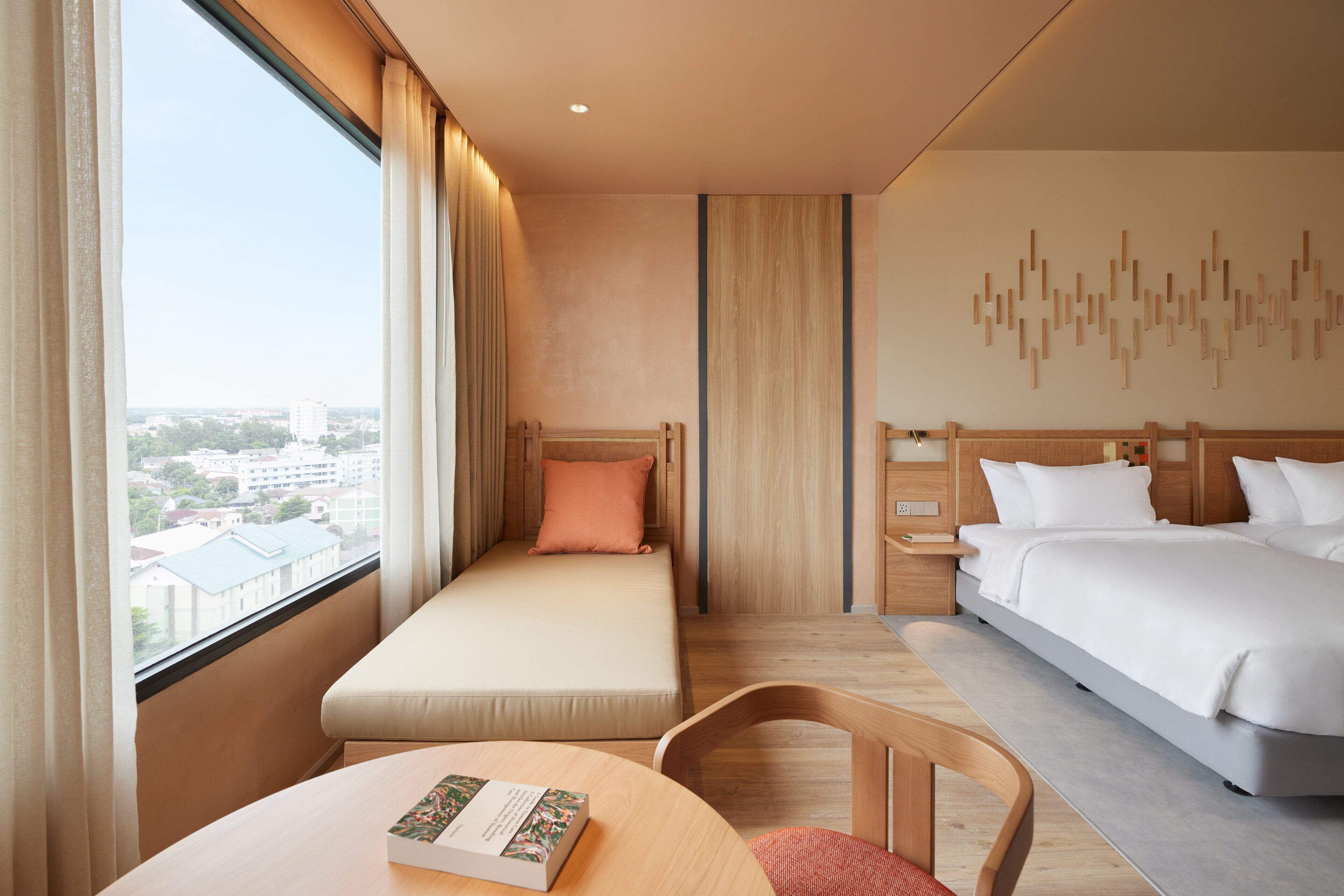 A hotel room with a bed, a sofa bed, a desk, and a view of the city.