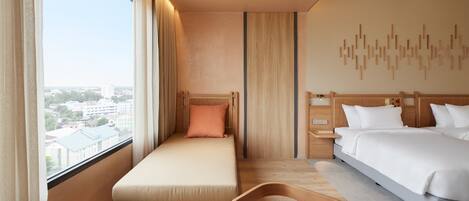 A hotel room with a bed, a sofa bed, a desk, and a view of the city.