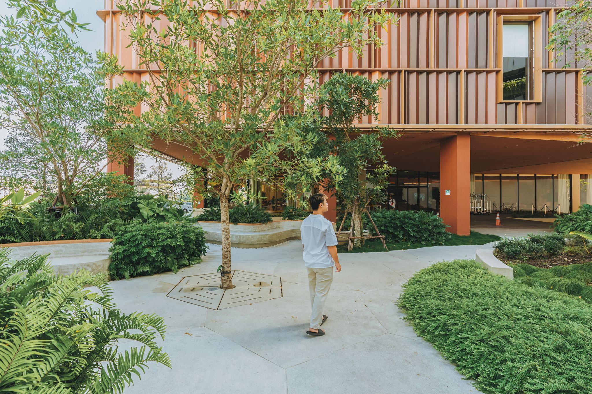 A man walking on a pathway in front of a building with a modern design, surrounded by greenery.